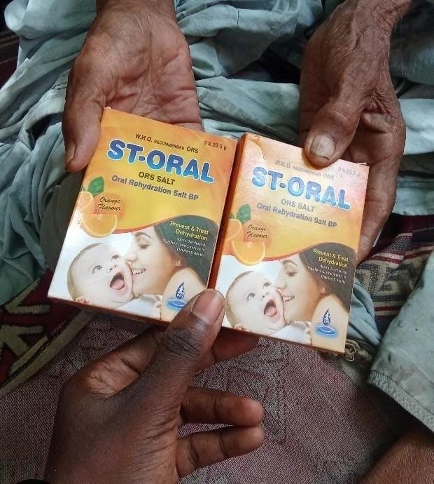 Two hands hold open two boxes of ST-ORAL oral rehydration salts, while a third, smaller hand reaches in from below to steady them.